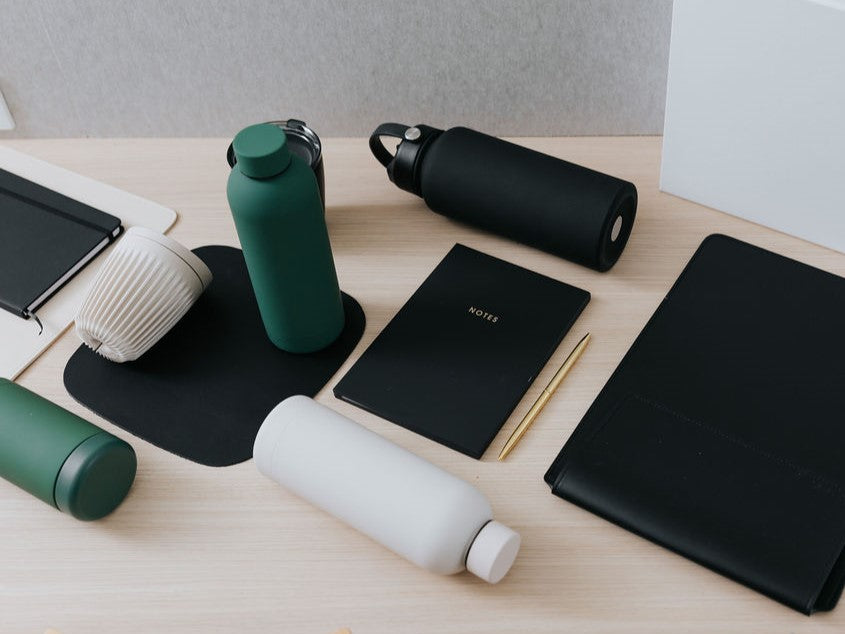 Parcelle | Custom Branded Merchandise Products including branded drink bottles, branded mouse pad, personalised vegan leather ipad holder, personalised notebook and branded pen on a desk
