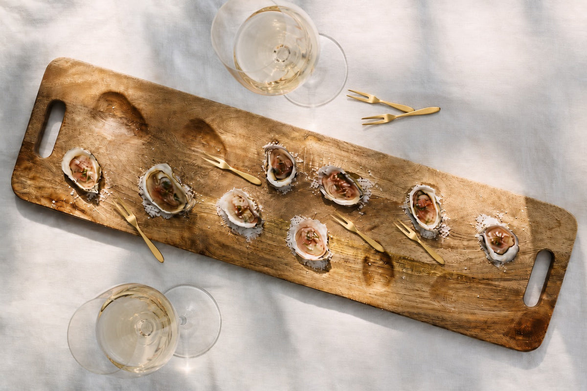 Parcelle timber oyster board with oysters, gold oyster forks and white wine on a linen tablecloth