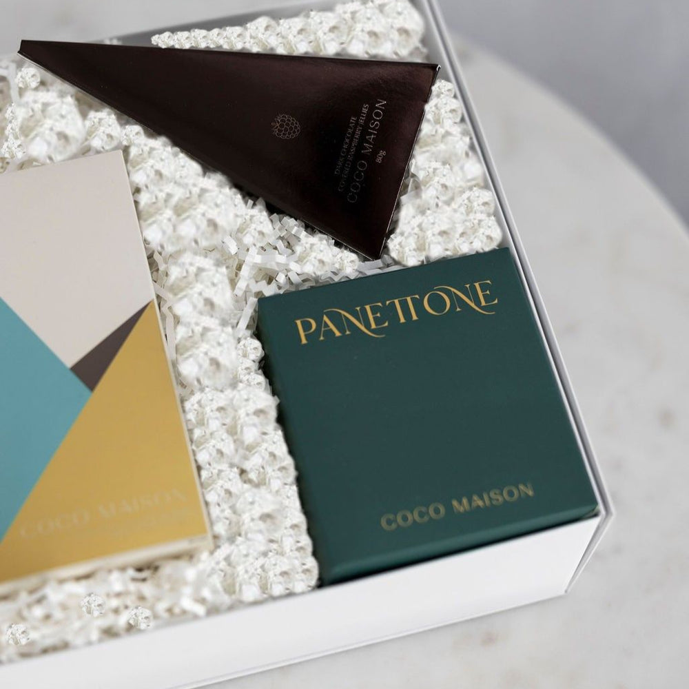 Parcelle | Inside view of Parcelle’s Be Festive Christmas hamper showing Pistachio Knafeh chocolate bar, mini Chocolate Chip Panettone, and Dark Chocolate Raspberry Jellies, elegantly packed in a signature gift box with festive sleeve